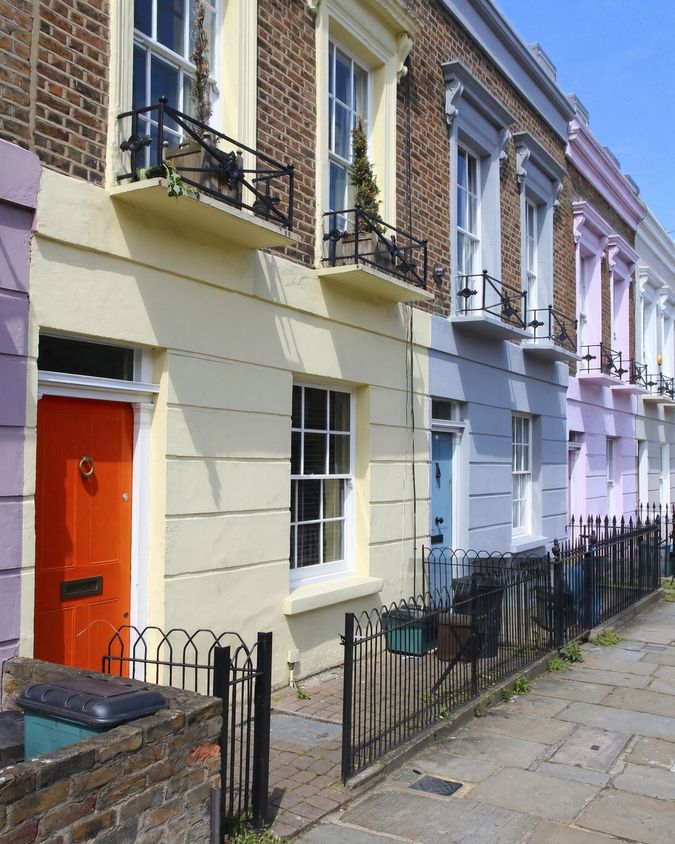 Row of terraced houses painted in soft pastel colours, with an orange front door, sash windows and black iron railings.