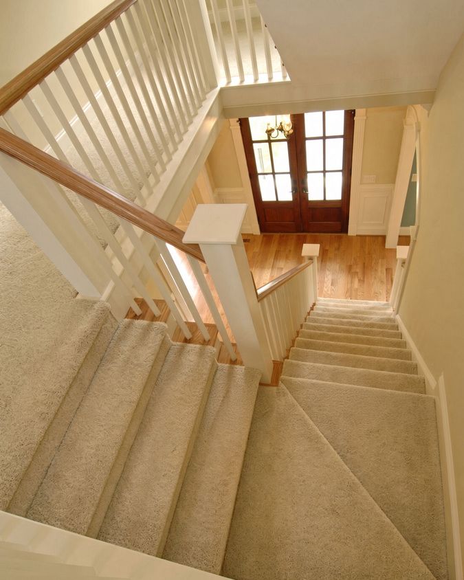 Stairwell with white painted walls and balustrades, cream carpeted stairs and a tall window at the half landing.