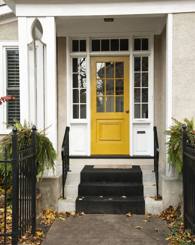 Front porch with a yellow panelled front door, white painted columns and woodwork, and black railings either side of the steps.